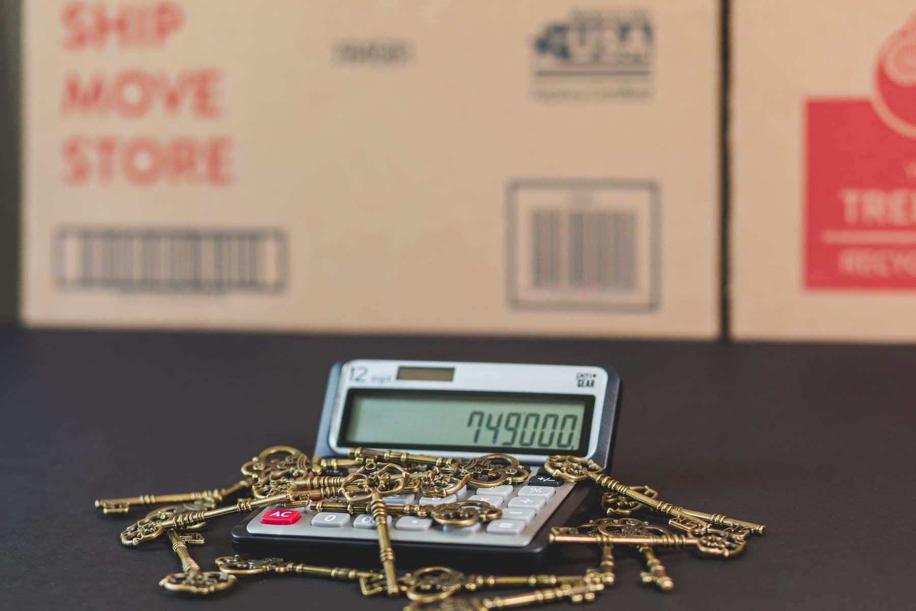 House keys resting on a calculator beside moving boxes